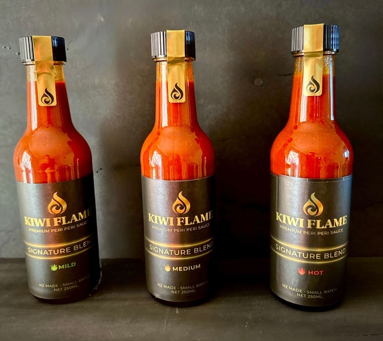 Kiwi Flame Mild, Medium and Hot bottles standing on a dark shelf