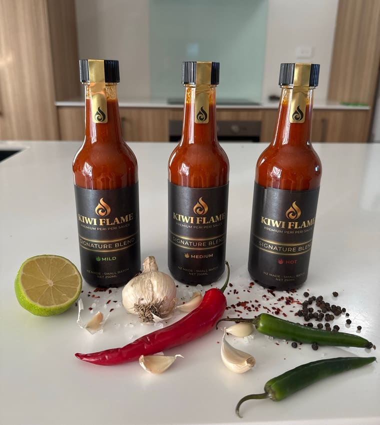 Mild, Medium and Hot bottles on a kitchen bench with chillies, garlic and peppercorns